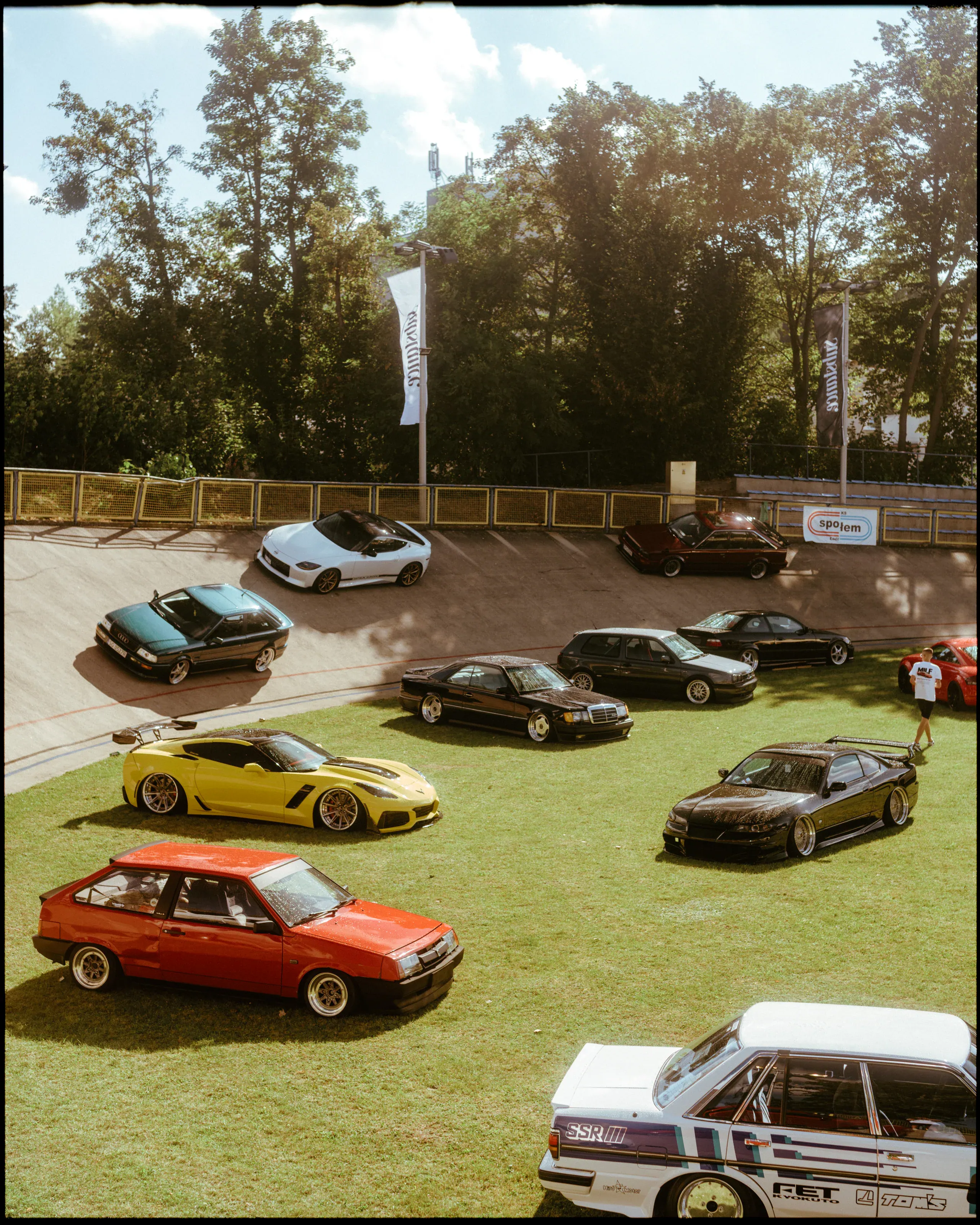 Overhead view of densely parked cars in many colours on a green field.