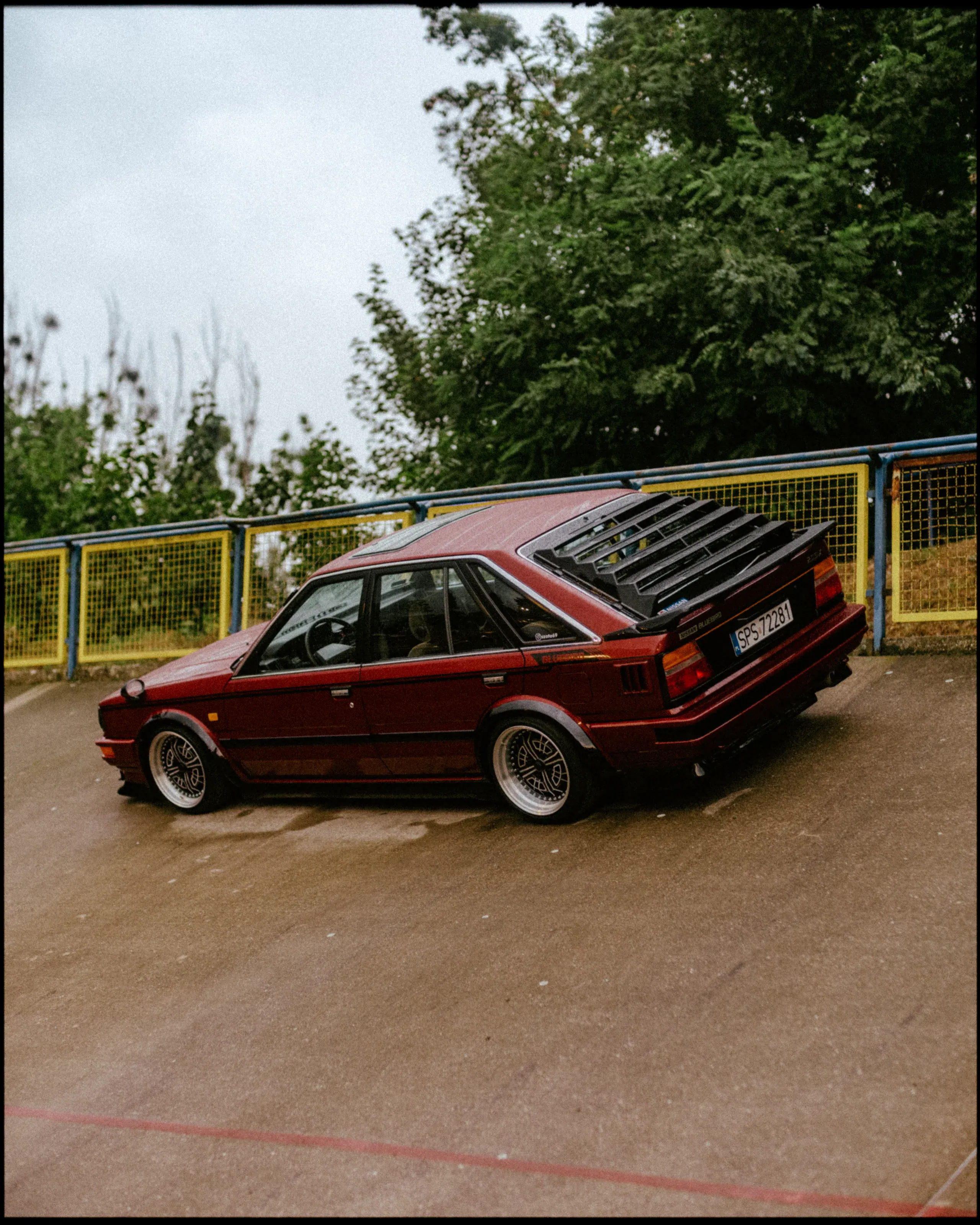 Red classic car turning on wet asphalt during the event.