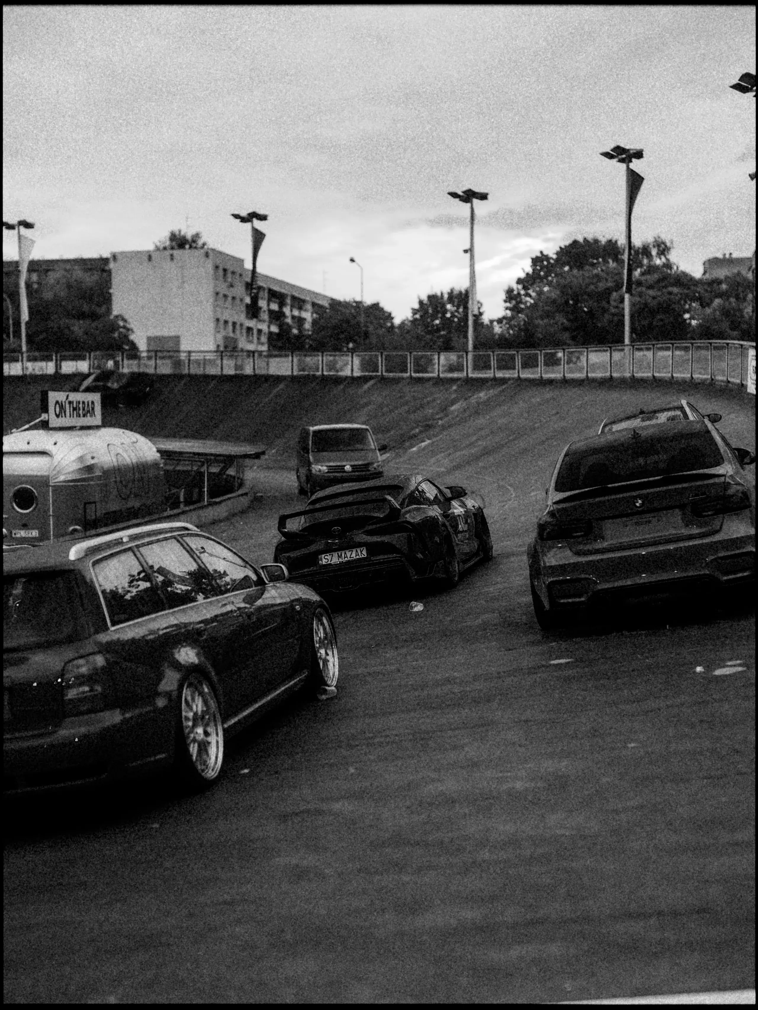 Black-and-white view of several cars entering the grounds of a motoring event.