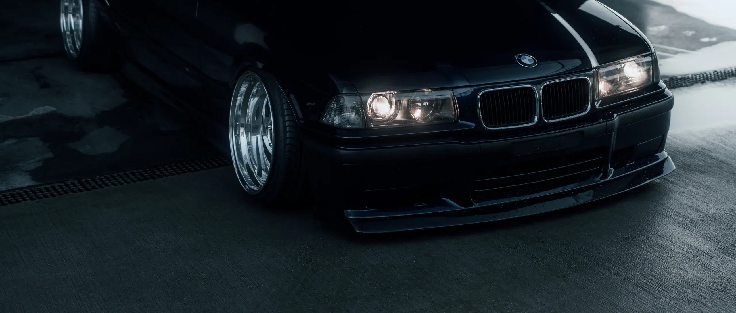 Ciemne BMW E36 przesuwające się przez mokry, betonowy parking.